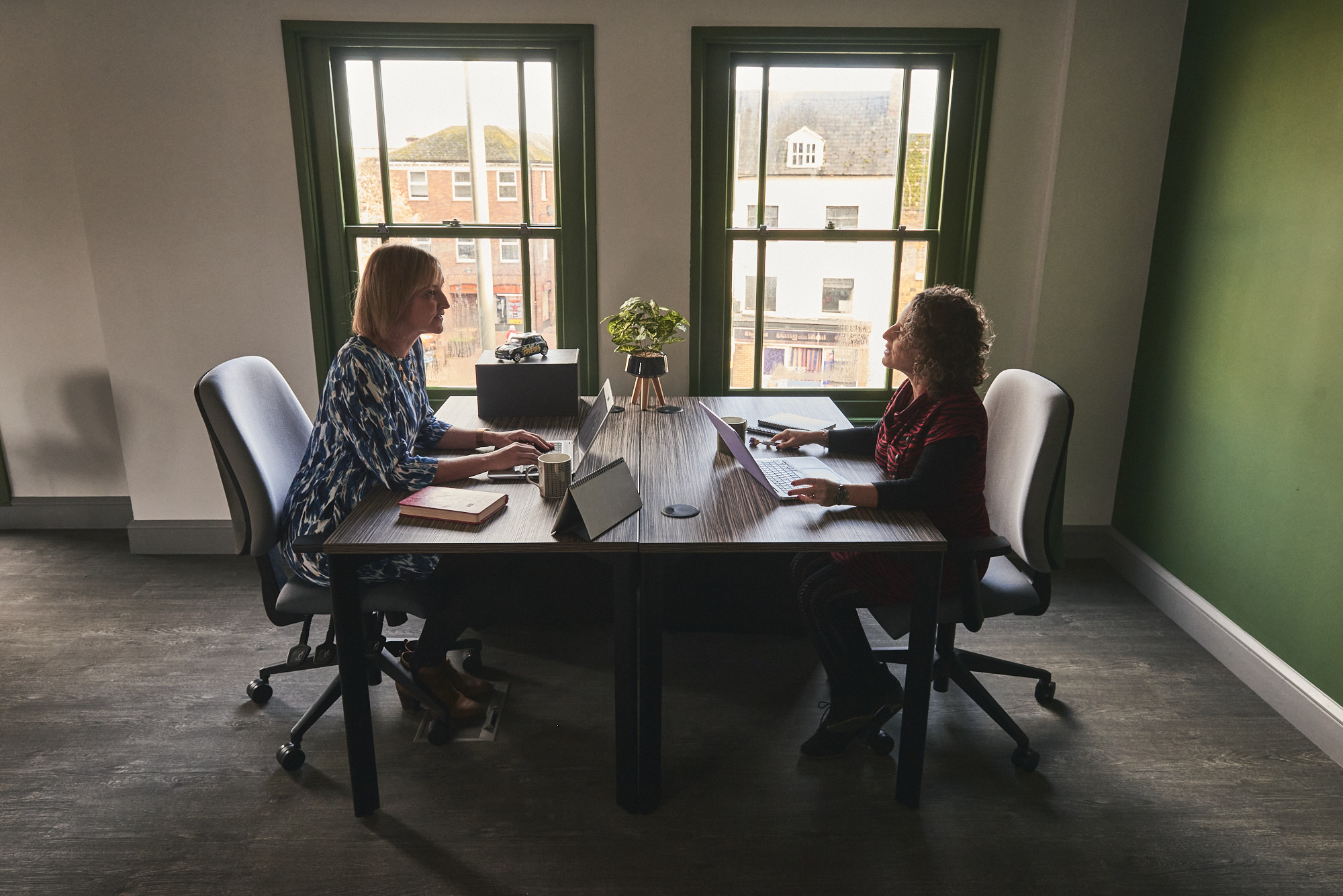 Two women sitting opposite at a wooden desk